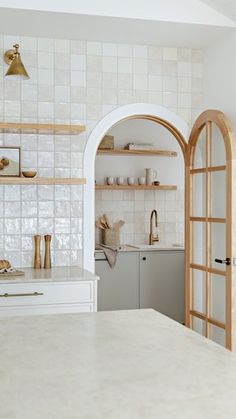 a white kitchen with open shelving and an arched doorway leading to the dining room