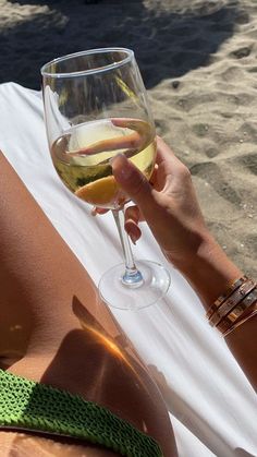 a woman laying on the beach with a glass of wine