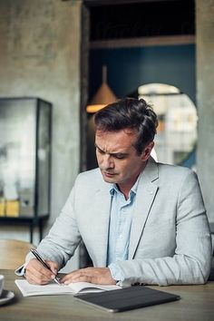 a man sitting at a table with a book and pen in his hand, writing