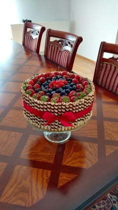 a cake sitting on top of a wooden table covered in berries and strawberries next to chairs