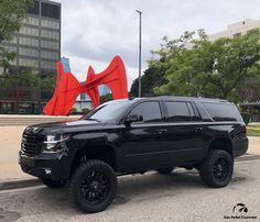 a black truck parked in front of a red sculpture