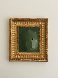 an empty gold frame hanging on the wall with a black dot in it's center