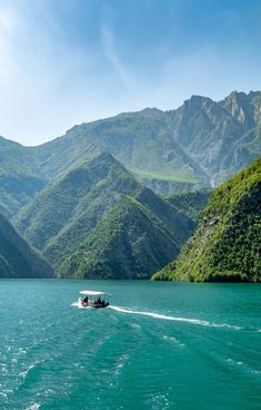 a boat is traveling through the water near some mountains and green trees in the background