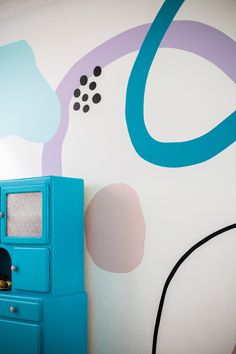 a blue cabinet is in front of a wall painted with circles and shapes on it