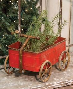 a red wagon filled with pine branches on top of a wooden table next to a christmas tree