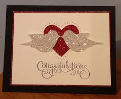 an congratulations card with two hearts and wings on the front, sitting on top of a wooden table