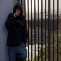 a young man leaning against a wall while talking on a cell phone