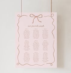 a pink and gold wedding seating plan hanging on a white wall with twine strings