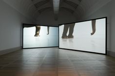 an empty room with two large screens on the wall and people's feet projected in them