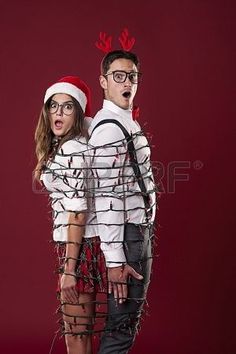 a man and woman dressed up as santa clause with christmas decorations on their head, standing in front of a red background