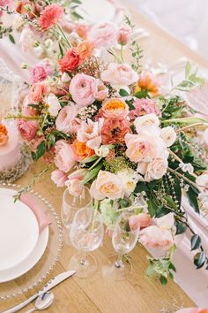 the table is set with pink and orange flowers in vases, silverware, and candles