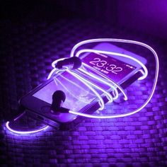 a cell phone is lit up with purple neon lights on the screen and charging cord