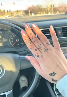 a woman's hand on the steering wheel of a car with stars and moon tattoos