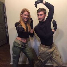 a man and woman posing for a photo in front of a wall with their hands up