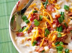 a white bowl filled with soup topped with cheese and green onions next to a spoon