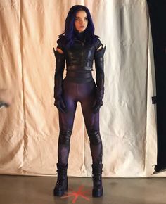 a woman with purple hair and black catsuits standing in front of a white backdrop