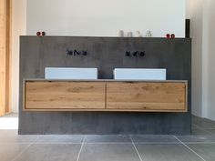 two white sinks sitting on top of a wooden cabinet next to a wall mounted faucet