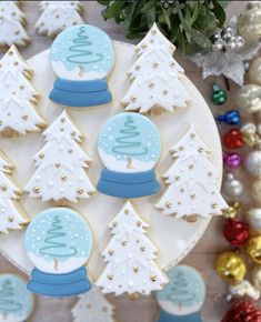 decorated cookies on a plate with christmas trees and snow globes in the middle, surrounded by other holiday decorations