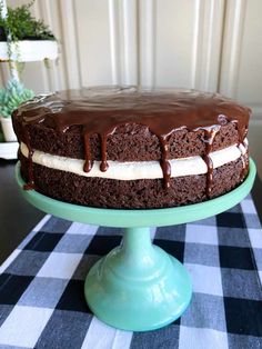 a chocolate cake with white frosting on a blue pedestal and checkered table cloth