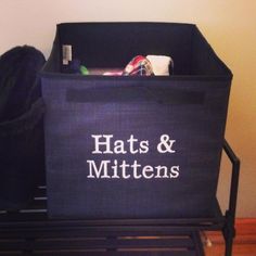 a black bin with the words hats and mittens on it next to a chair