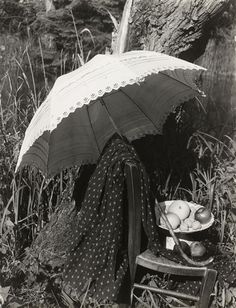 an old black and white photo of a woman sitting in the grass with an umbrella over her head