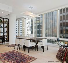 the dining room table is surrounded by chairs and rugs in front of large windows