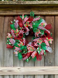 a christmas wreath hanging on the side of a wooden fence with green and red ribbons