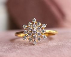 a diamond ring sitting on top of a pink velvet covered surface, with the center stone surrounded by small white diamonds