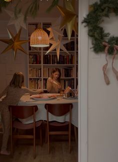 two women sitting at a table in front of bookshelves with christmas decorations hanging from the ceiling