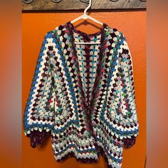 a colorful crocheted sweater hanging on a wooden hanger next to an orange wall