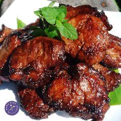 some meat is sitting on a white plate with green leafy garnishes