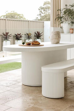 a white table with two benches in front of it and potted plants on the other side