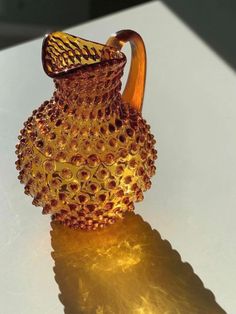 a yellow glass vase sitting on top of a white table next to a light fixture