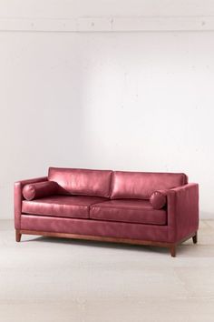 a red leather couch sitting on top of a hard wood floored floor next to a white wall