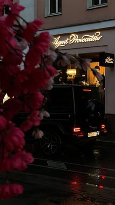 a car parked in front of a building on a wet street with flowers hanging from it's roof