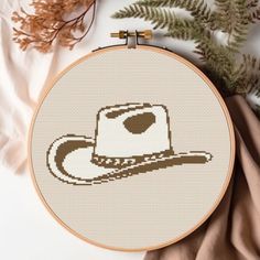 a cross stitch pattern with a cowboy hat on it next to some plants and leaves