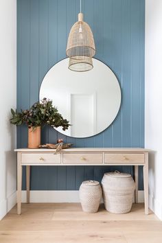 a mirror on the wall next to a table with two baskets and a potted plant