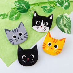 three cat magnets sitting on top of a green leafy plant next to each other