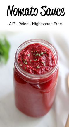 a jar filled with red sauce sitting on top of a white table next to a wooden spoon