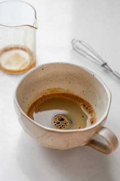 a coffee cup filled with liquid next to a whisk on a counter top