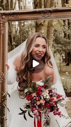 a woman standing in front of a mirror with a bouquet on her wedding day and smiling at the camera