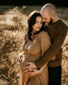 a pregnant couple cuddles in the tall grass while holding each other's belly