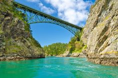 a bridge that is over some water in the middle of a mountain range with green trees