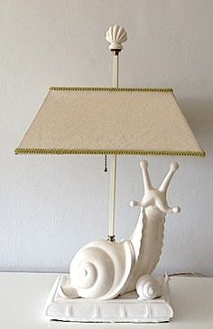 a lamp that is sitting on top of a table with a snail underneath it and a shell under the shade