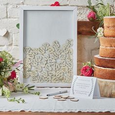 a table topped with lots of cake next to a white frame and red flowers on top of it