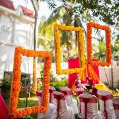 an outdoor ceremony with orange and yellow flowers in the shape of square frames hanging from strings