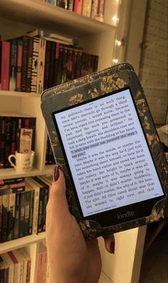 a person holding an electronic device in front of a book shelf with books on it