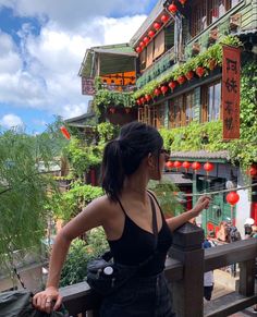 a woman standing on top of a balcony next to a building with red lanterns hanging from it