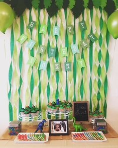 a table topped with lots of green desserts and balloons in front of a party banner