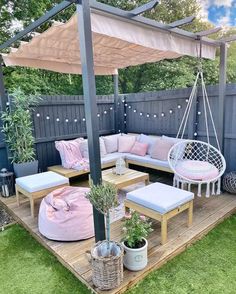 an outdoor patio with furniture and plants on the deck, in front of a wooden fence